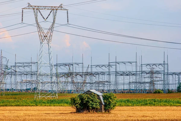 Arka plandaki elektrik santralinden gelen büyük elektrik direkleri tarladaki küçük ahır binasını çevreliyorlar.