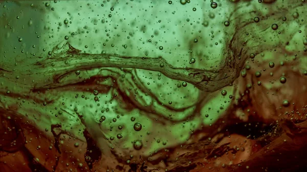 Threads of red ink trapped between green dish soap detergent.