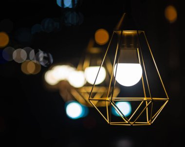 Yan yana asılı çoklu geometrik demir klasik lamba gölgeleri. Karanlık sokak gece fotoğrafçılığı. Restoran verandası gece hayatı. Arka planda yuvarlak bokeh.