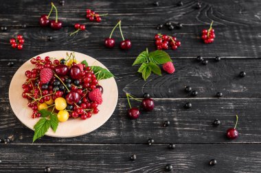 Ahududu, kiraz, frenk üzümü, karanlık bir arka plan karşı ahşap bir tabakta blackcurrant. Arka plan olarak kullanılabilir