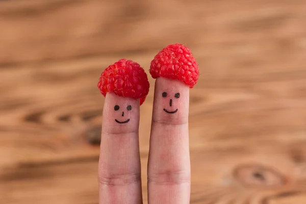 Two smiling faces drawn on fingers in caps from raspberry