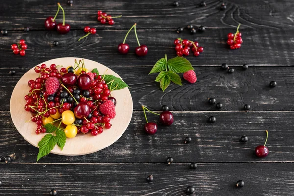 Ahududu, kiraz, frenk üzümü, karanlık bir arka plan karşı ahşap bir tabakta blackcurrant. Arka plan olarak kullanılabilir