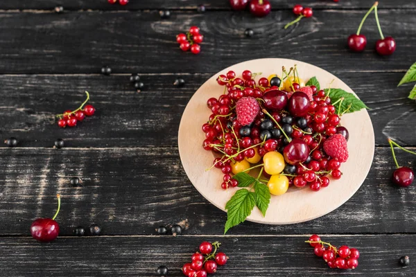 Ahududu, kiraz, frenk üzümü, karanlık bir arka plan karşı ahşap bir tabakta blackcurrant. Arka plan olarak kullanılabilir