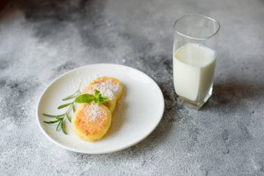 Lezzetli taze peynir krep ile bir bardak süt bir beton zemin üzerine beyaz bir plaka üzerinde. Sağlıklı ve diyet kahvaltı