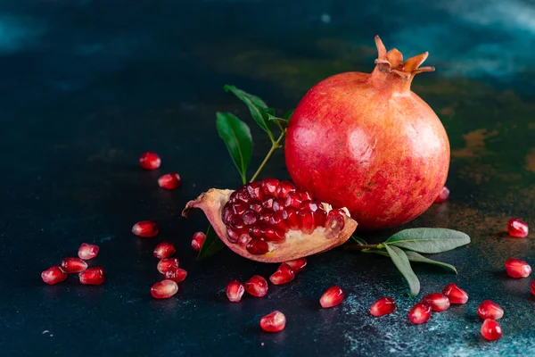 Red juice pomegranate on dark background. Ripe pomegranate with leaves on a dark background