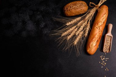 Tahıllar ve koyu bir arka plan karşı buğday konileri ile taze kokulu ekmek. Ahşap masa arka plan üzerinde pişmiş ekmek çeşitleri. Masada taze kokulu ekmek var. Gıda konsepti. 