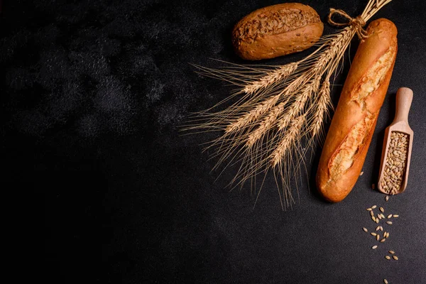 Tahıllar ve koyu bir arka plan karşı buğday konileri ile taze kokulu ekmek. Ahşap masa arka plan üzerinde pişmiş ekmek çeşitleri. Masada taze kokulu ekmek var. Gıda konsepti. 