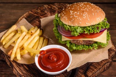 Sığır eti, domates, peynir, salatalık ve marul ile lezzetli ızgara ev yapımı burger. Lezzetli ızgara burgerler. Ahşap masada zanaat sığır burger ve patates kızartması