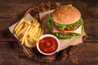 Sığır eti, domates, peynir, salatalık ve marul ile lezzetli ızgara ev yapımı burger. Lezzetli ızgara burgerler. Ahşap masada zanaat sığır burger ve patates kızartması