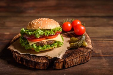 Sığır eti, domates, peynir, salatalık ve marul ile lezzetli ızgara ev yapımı burger. Lezzetli ızgara burgerler. Ahşap masada zanaat sığır burger ve patates kızartması