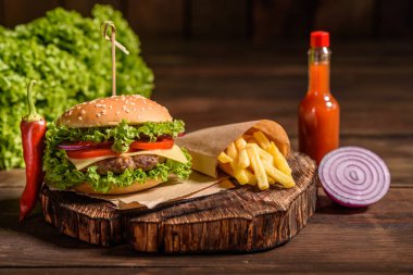 Sığır eti, domates, peynir, salatalık ve marul ile lezzetli ızgara ev yapımı burger. Lezzetli ızgara burgerler. Ahşap masada zanaat sığır burger ve patates kızartması
