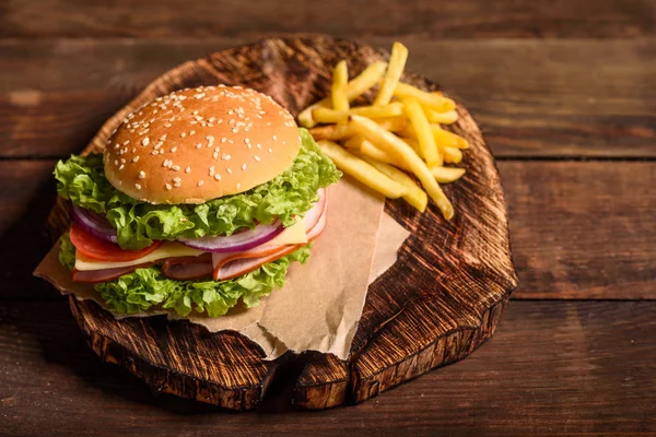 Tasty grilled homemade burger with beef, tomato, cheese, cucumber and lettuce. Delicious grilled burgers. Craft beef burger and french fries on wooden table