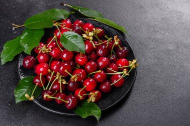 Olgun kiraz yığınını yaprak ve saplarla kapatın. Büyük bir taze kırmızı kiraz koleksiyonu. Olgun kiraz arkaplanı