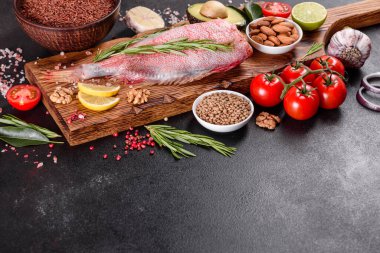 Koyu bir arka planda baharat ve otlarla pişirmek için hazırlanmış ham kızıl deniz filetosu.