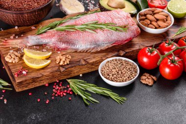 Koyu bir arka planda baharat ve otlarla pişirmek için hazırlanmış ham kızıl deniz filetosu.