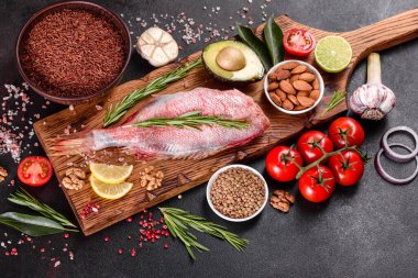 Koyu bir arka planda baharat ve otlarla pişirmek için hazırlanmış ham kızıl deniz filetosu.