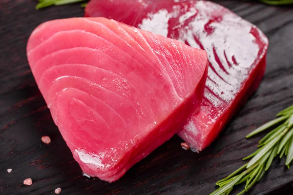 Fresh tuna fillet steaks with spices and herbs on a black background. Preparing tuna for baking