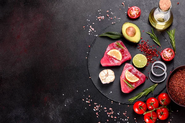 Fresh tuna fillet steaks with spices and herbs on a black background. Preparing tuna for baking