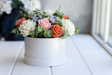 Hediye silindirik karton bir kutuda güzel, parlak gül çiçekleri. Bir buket sabun çiçeği.