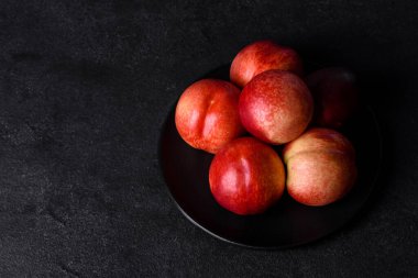Lezzetli tatlı şeftaliler ya da kahverengi bir kasede koyu beton bir arka planda nektarinler.