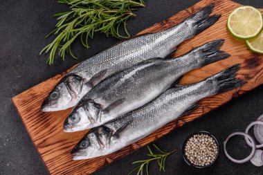 Taze balık deniz kabuğu ve yemek pişirmek için malzemeler. Koyu bir masada baharat ve bitkilerle çiğ balık deniz kabuğu.