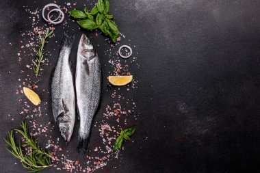 Taze balık deniz kabuğu ve yemek pişirmek için malzemeler. Koyu bir masada baharat ve bitkilerle çiğ balık deniz kabuğu.