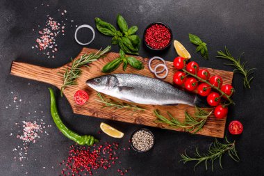 Taze balık deniz kabuğu ve yemek pişirmek için malzemeler. Koyu bir masada baharat ve bitkilerle çiğ balık deniz kabuğu.