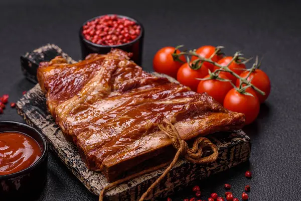 Delicious smoked or grilled ribs with olives, spices and herbs on a dark concrete background