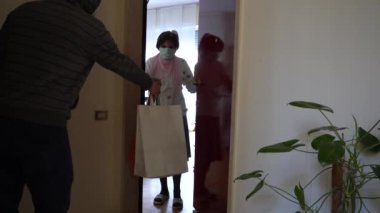 Avrupa, İtalya, Milano Aralık 2020 - Maskeli kadın, Covid-19 Coronavirus 'un kilit altına alınması sırasında ev kapısının önündeki paketleri aldı
