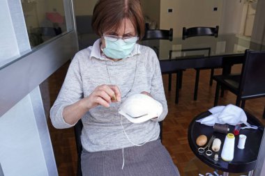 Avrupa, İtalya, Milano - 70 yaşındaki karantina maskeli kadın kendini salgın N-cov19 Coronavirus 'tan korumak için iç etkinlik yapıyor - maskesini dikin ve antivirüs onarımını yapın