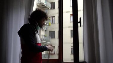 Pencerenin yanında duran maskeli genç adam.