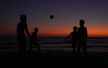 Gün batımında sahilde insan siluetleri.