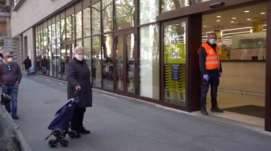 EUROPE, ITALY, MILAN Mart 2020 - Coronavirus salgını sırasında Giambellino, Lorenteggio 'da yaşam stili - süpermarket görevlisi maskeli insan kuyruğunu 1 metre uzaklıktan ayarlar