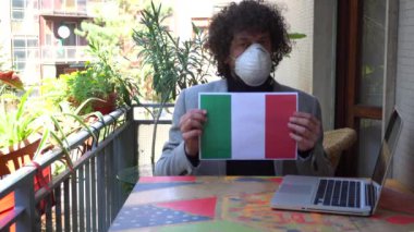 Avrupa, İtalya, Milano - İnsan 40 yaşında evde maske takıyor 19 Coronavirus salgını karantinası sırasında - evde çalışıyor ve İtalya bayrağının enfekte olduğunu gösteriyor