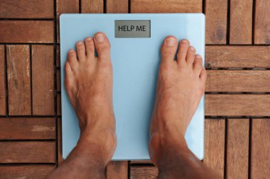 Üzerinde dengesi yazan akıllı terazilerin üzerinde duran yalınayak bir adamın en üst görüntüsü. Aman Tanrım. Gri ahşap zeminde duran boş dengeli beyaz ağırlıklar.