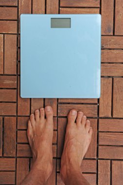 Üzerinde dengesi yazan akıllı terazilerin üzerinde duran yalınayak bir adamın en üst görüntüsü. Aman Tanrım. Gri ahşap zeminde duran boş dengeli beyaz ağırlıklar.