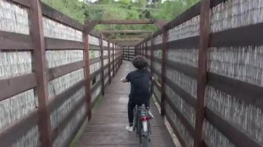 Yaz ormanında tahta köprüde bisiklet süren bir çocuğun arka manzarası. 