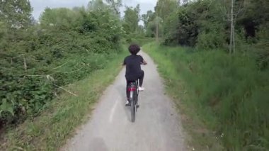 Yaz ormanında bisiklet süren bir çocuğun arka manzarası. 