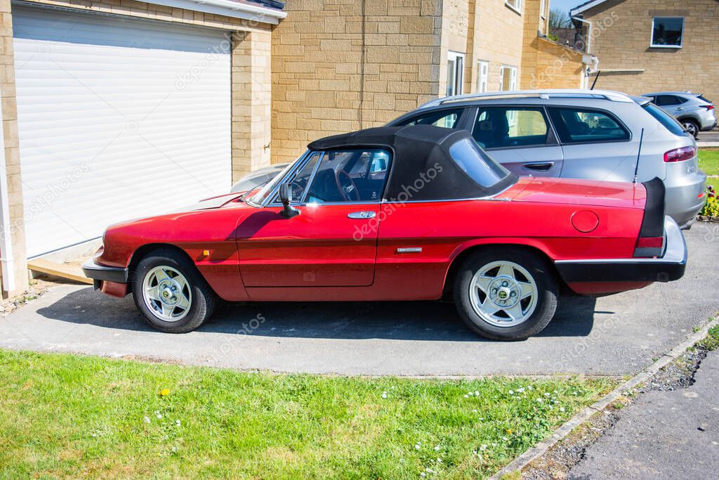 A red Alfa-Romeo spider, 2 seater sports car, parked on a driveway in front of a garage door