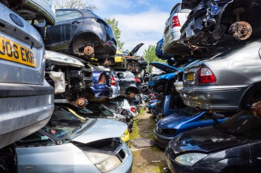 Cars with their wheels removed are stacked in rows of piles of 3 cars with paths between them in a breakers scrap yard clipart