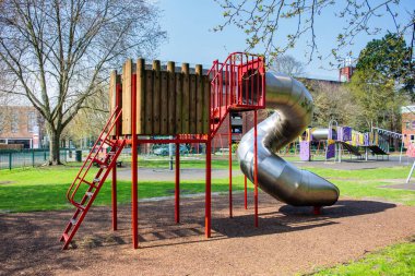 Trowbridge şehir parkının çocuk oyun alanında arka planda diğer ekipmanlarla birlikte metal kıvrımlı bir tirbuşon tüp kayması.