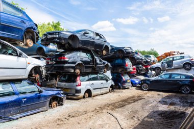 Cars with their wheels removed are stacked in piles of 3 cars with paths between them in a breakers scrap yard clipart