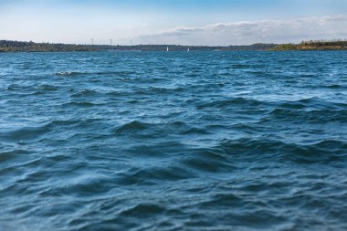Wunderschoene Sommerlandschaft auf dem See, tiefblaues Wasser, mit kleinen Wellen und kleinem Wald auf dem Land.
