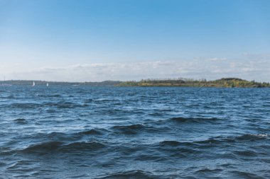 Wunderschoene Sommerlandschaft auf dem See, tiefblaues Wasser, mit kleinen Wellen und kleinem Wald auf dem Land.