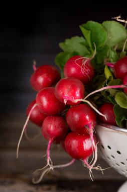 Taze ıslak turp üzerinde beyaz kevgir içinde eski bir ahşap masa. Köy tarzı. Karanlık anahtar fotoğraf.