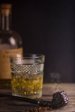 Koyu kahverengi yasaktır boru ve ahşap masa üzerinde uzun bardak viski oyma tütün.