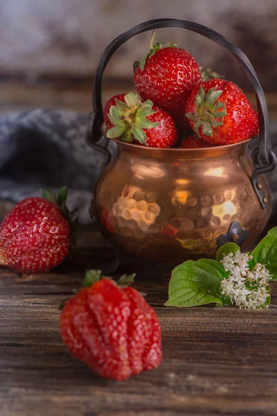 Ahşap bir masa üzerinde bakır bir kapta büyük kırmızı çilek.