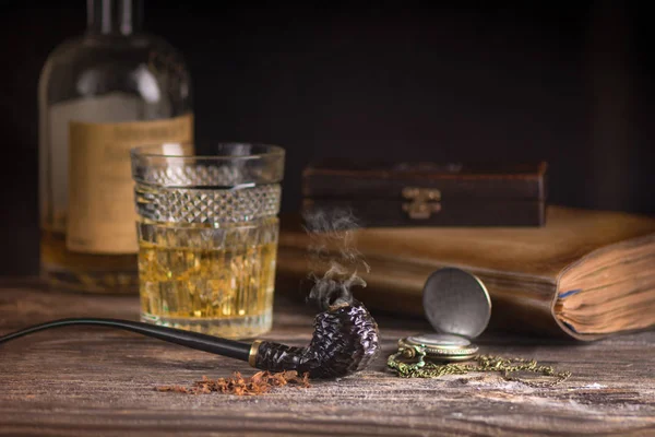 Koyu kahverengi yasaktır boru ve ahşap masa üzerinde uzun bardak viski oyma tütün.