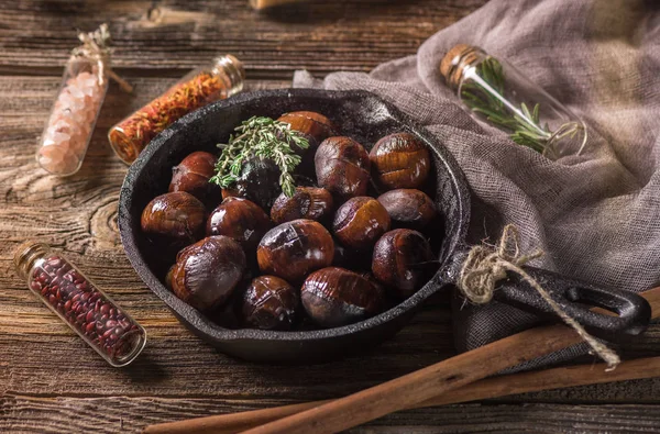 Kestane. Koyu ahşap masa üzerinde dökme demir tavada kavrulmuş yenilebilir kestane hizmet.