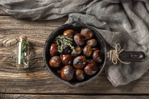 Kestane. Koyu ahşap masa üzerinde dökme demir tavada kavrulmuş yenilebilir kestane hizmet.
